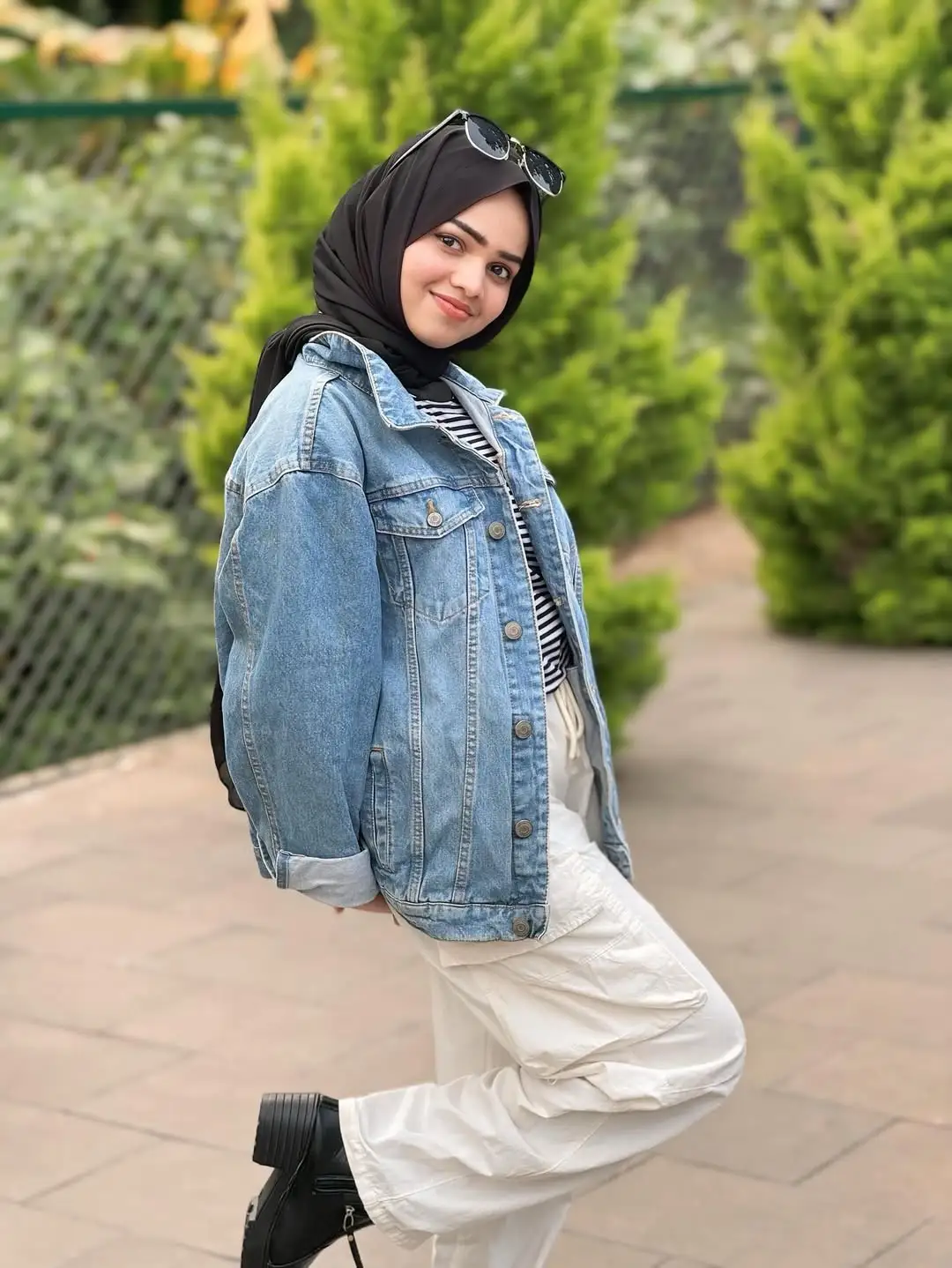 Best SEO Expert in Kochi smiling outdoors in a black hijab, striped top, and denim jacket with a blurred green pathway in the background.